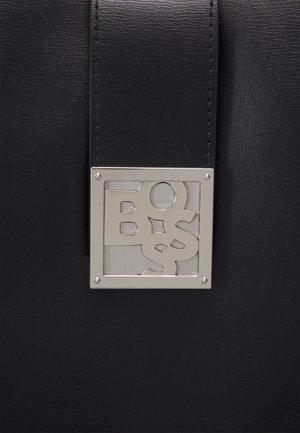 Černý kožený povrch s vertikálním prošitým pruhem a čtvercovou stříbrnou kovovou růžkou se stylizovanými vyřezávanými písmeny.