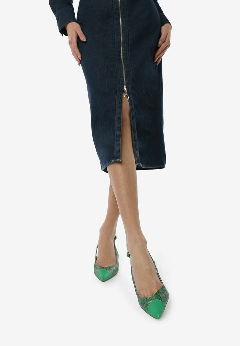 Bailarinas verdes de punta con un diseño de estampado de serpiente texturizado y una puntera verde sólida. Se llevan con un vestido de mezclilla ajustado con cremallera frontal.