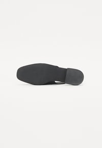Sapatilha preta com bico arredondado, design fácil de calçar e sola de borracha texturizada com riscas horizontais para melhor aderência.