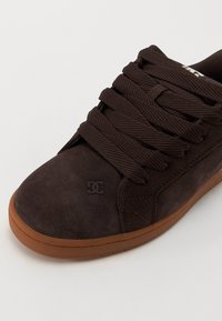 Braune Wildleder-Sneaker mit dicken Schnürsenkeln und einer Gummisohle. Verfügt über ein dunkles Logo an der Seite und eine glatte Textur für ein elegantes Design.