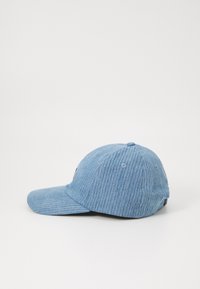 Șapca albastră din corduroy are o visieră curbată, o textură fină cu nervuri, găuri de ventilație pe lateral și o etichetă cu logo pe față.