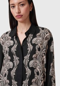 Blusa nera con un intricato motivo paisley in beige e crema, dotata di colletto e chiusura con bottoni, realizzata in tessuto leggero.
