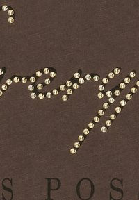 Brun stof med dekorative guld nitter arrangeret i kursiv skrifttype, samt fed sort tekst nederst.