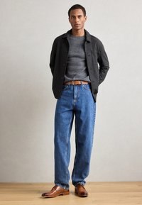 Maglione grigio a maglia, giacca button-up grigio scuro, jeans blu a vestibilità rilassata, cintura in pelle marrone e scarpe eleganti marroni. Design semplice e funzionale.