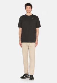 T-shirt nera in cotone a maniche corte con logo ricamato, abbinata a pantaloni tapered beige chiaro e scarpe da ginnastica nere.