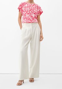 Top rosa a maniche corte con motivo floreale abbinato a pantaloni bianchi a gamba larga e sandali con tacco nudo. Il tessuto ha una consistenza liscia.