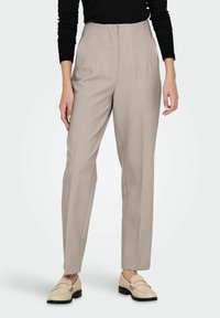 Pantalon beige clair cintré avec une taille haute, coupe droite et texture subtile. Associé à des mocassins crème pour un look complet.