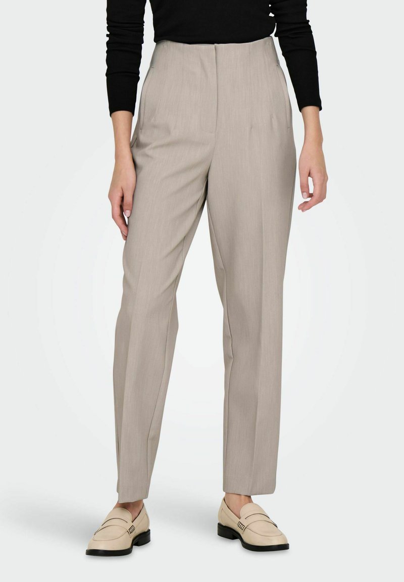 Pantalon beige clair cintré avec une taille haute, coupe droite et texture subtile. Associé à des mocassins crème pour un look complet.