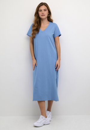 Relaxed-fit V-neck dress in light blue cotton, knee-length, short sleeves, with side slits and a raw hem. Paired with white sneakers.
