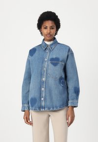 Lys blå denimskjorte med knapfront, krave, lomme medlapp og hjerteformede blegespor. Lange ærmer med manchetter.