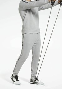 Grå ribbad träningsoverall med långa ärmar och byxor, med svarta sidostreck. Modellen håller i träningsmotståndsband med handtag.