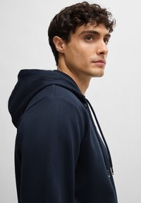 Sweatshirt azul-marinho com capuz ajustável, tecido suave e detalhes de costura discretos, visto de lado em um fundo liso.