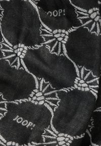 Tissu noir avec un motif floral répété en blanc. Le design inclut le mot "JOOP!" intégré dans l'impression.