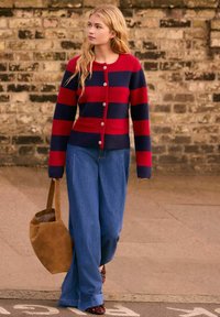 Randig cardigan i röd och marinblå med knäppning, försedd med två framfickor. Matchas med lösa jeansbyxor och en beige mockaväska.