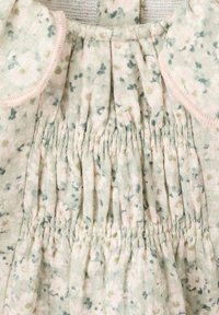 Abito con motivo floreale su una base verde morbida. Presenta dettagli arricciati e profili rosa lungo il collo e le maniche. Tessuto testurizzato.