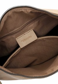 Tan fabric bag interior with a zippered pocket and a smooth leather tag featuring the brand name "Tamaris." Zipper detail visible along the edge.