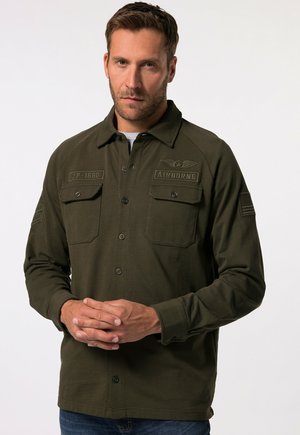 Koszula w stylu militarnym w ciemnooliwkowym kolorze, z zapięciem na guziki z przodu, dwiema kieszeniami na piersi i haftowanymi naszywkami na ramionach.