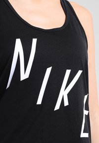 Czarny top na ramionkach wykonany z miękkiego materiału, z dużym białym logo "NIKE" w nowoczesnej czcionce. Okrągły dekolt, bez rękawów.