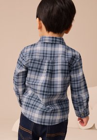 Kék kockás hosszú ujjú pamut ing sötétkék, világoskék és fehér csíkokkal. A hátsó rész részletezése gallért és gombos mandzsettákat tartalmaz.
