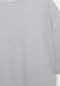 T-shirt en coton gris clair avec un col rond et des manches courtes. Texture lisse avec des détails de couture visibles.