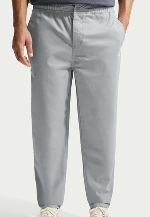 Mężczyzna noszący jasno-szare, casualowe spodnie z elastycznym pasem i bocznymi kieszeniami, w połączeniu z białymi trampkami.