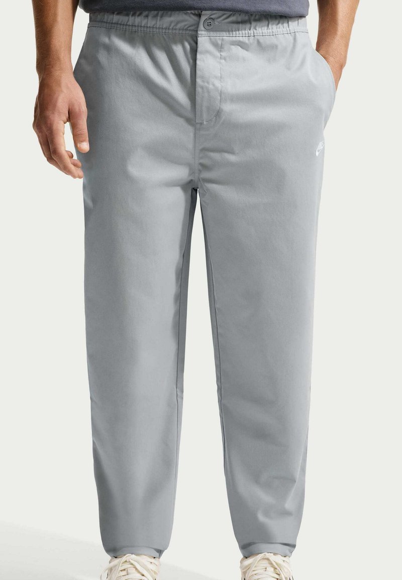 Uomo che indossa pantaloni casual grigio chiaro con elastico in vita e tasche laterali, abbinati a scarpe da ginnastica bianche.