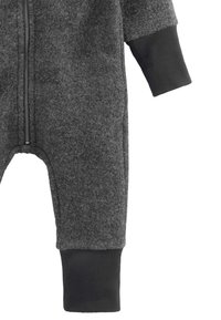 Grijze fleecen baby jumpsuit met een rits aan de voorkant, ribbelige zwarte manchetten op de mouwen en benen, tegen een witte achtergrond.