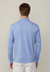 Langarm-Polohemd aus leichtem blauen Baumwollstoff, mit Kragen, knöpfbaren Manschetten und geradem Saum. Glatte Textur und schlichtes Design.