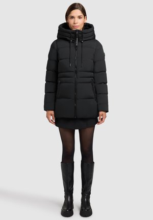 Sort puffjakke med hætte, der har lynlås foran og to sidelommer. Materialet ser blødt ud med et quiltet design og en elegant overflade.
