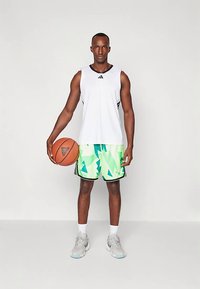 Fehér, ujjatlan sportmez fekete részletekkel; zöld mintás kosárlabdazs shorts; kosárlabdát tart a kezében; világosszürke sportcipőt visel.