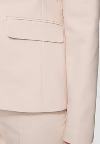 Lichtroze op maat gemaakte blazer met een zachte textuur, een enkele borstzak en gestructureerde mouwen, geschikt voor formele gelegenheden.