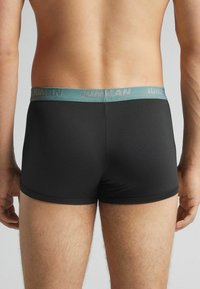 Bóxer negro con una textura suave y una cinturilla color teal que presenta el nombre de la marca impreso en gris. Diseño simple y funcional.