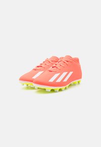 Scarpe da calcio di un brillante colore corallo con strisce bianche, tomaia sintetica e suole gialle, caratterizzate da un design con lacci e tacchetti stampati.