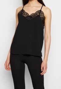 Camisole noire avec bordure en dentelle au niveau du décolleté, bretelles spaghetti réglables et coupe décontractée. Texture lisse, dos avec superposition.