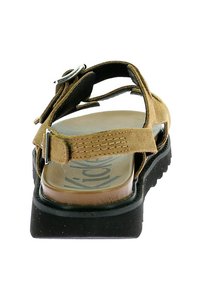 Brun mocka sandal med flera remmar och silverfästen, bestående av en texturerad innersula och en tjock svart yttersula.