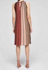 Robe mi-longue avec des rayures verticales dans les tons de rouge, beige et marron. Matière tricot douce avec un détail à nouer au niveau du col.