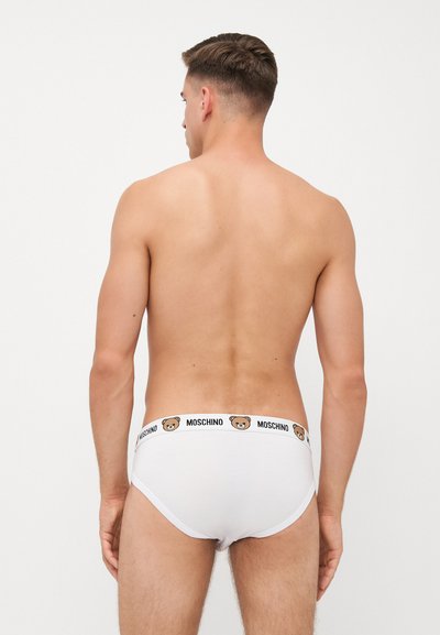 Weiße Baumwollslips mit einem schwarzen, gebrandeten Gummibund, der ein Bärenmotiv zeigt. Glatte Textur und enganliegendes Design.