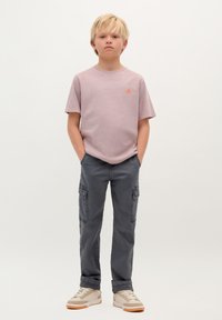 T-shirt di cotone rosa chiaro con logo arancione, abbinata a pantaloni cargo grigi con tasche e una vestibilità rilassata. Sneakers beige con un design testurizzato.