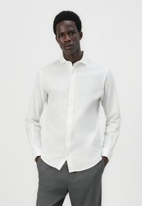 White long-sleeve button-up shirt with a standard collar, featuring a smooth texture and slender fit, paired with gray trousers.