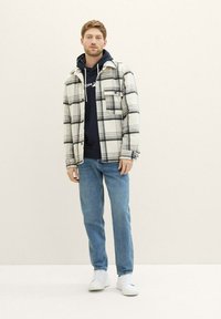 Biała koszula flanelowa w czarną kratę, założona na granatowy hoodie. Dżinsy oraz białe trampki dopełniają zestaw. Swobodny i warstwowy wygląd.