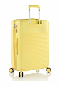 Valigia rigida gialla con texture a righe verticali, doppie ruote, manico telescopico e chiusura a zip.