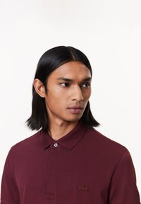 Burgunderröd polo tröja i strukturerad tyg, med klassisk krage och en knapp, samt en liten broderad logotyp på bröstet.