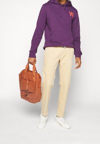 Fialová mikina s kapucí, béžové kalhoty, bílé tenisky a oranžová látková taška s horními uchy a předním klopou.