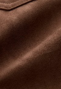 Material din suede maro, cu o suprafață moale și texturată, care prezintă o culoare bogată și uniformă, având un luciu ușor. Materialul are o finisare netedă și mat.