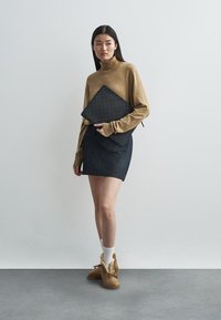 Barna turtleneck pulóver, sötét farmer szoknya és szőrme díszítésű barna mamusz. Fekete steppelt laptop-táska van a kezében. Egyszerű, modern dizájn.