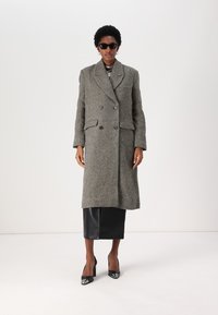 Abrigo de gran tamaño en patrón de espiga gris con diseño de doble botonadura, gran cuello con muescas y bolsillos laterales, combinado con una falda de cuero negra.