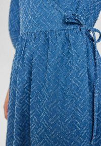 Zila denim kleita ar teksturētu zīda raibumu rakstu, izsistām vidukli un saitītes detaļu. Mīksta auduma, ar brīvu piegriezumu.