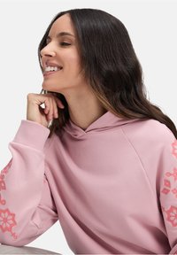 Felpa rosa con una texture morbida, dotata di cappuccio e motivi corallo decorativi sulle maniche. Vestibilità casual con maniche a raglan.
