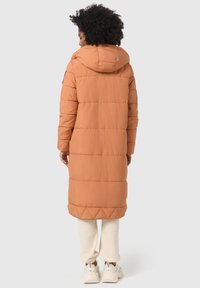 Lange, oranje pufferjas met een capuchon. Heeft een gestikt ontwerp en zijzakken, gecombineerd met witte broek en sneakers.