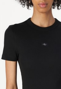 T-shirt nera a costine con maniche corte e colletto rotondo. Caratterizzata da un piccolo logo nero e argento sulla parte anteriore. Texture morbida.